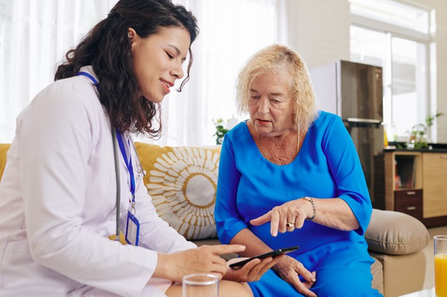 Geriatra lendo um mobile com uma senhora de vestido azul.